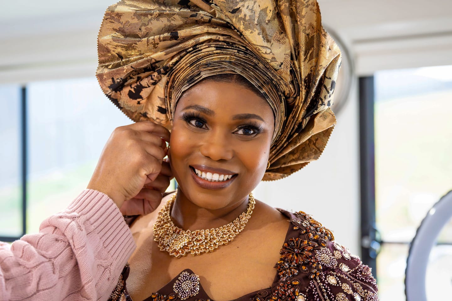 A final adjustment to an earring before the shoot, gold gele wrapped high and a heavy gold choker in place