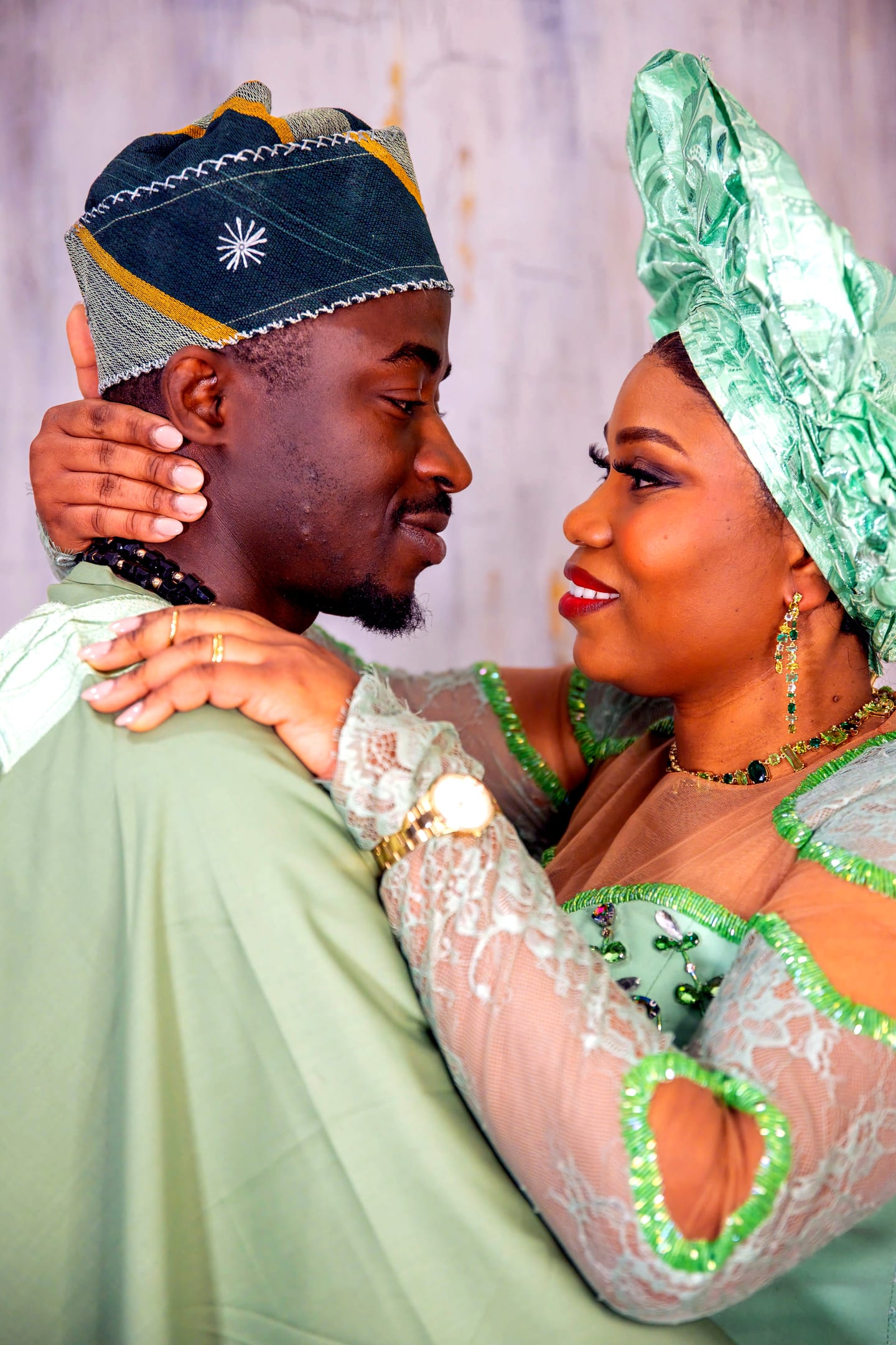 A couple in matching sage green attire holding each other close, gazing into each other's eyes