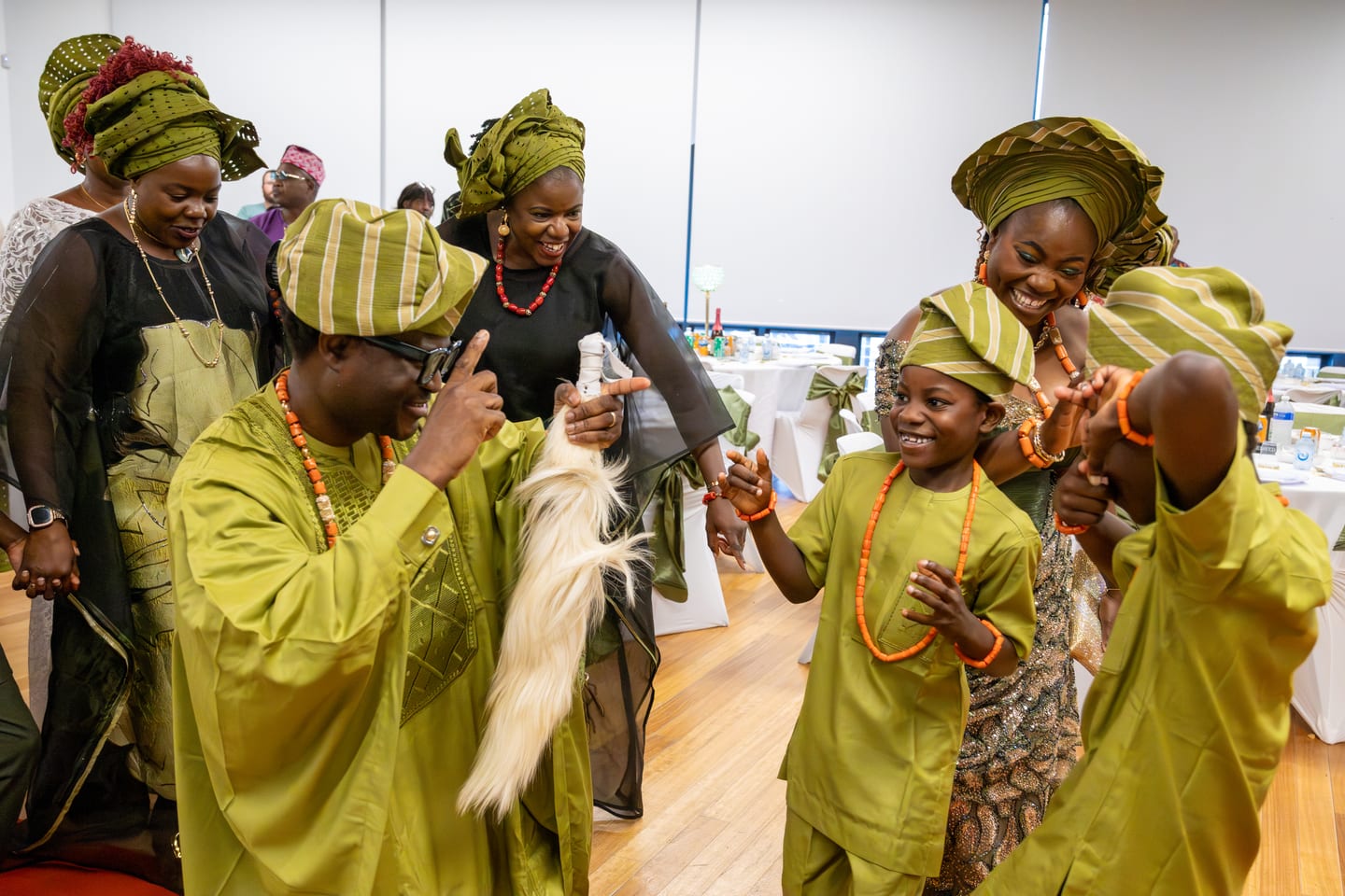 Guests of three generations dancing together in green and gold, one man waving a white horsetail whisk