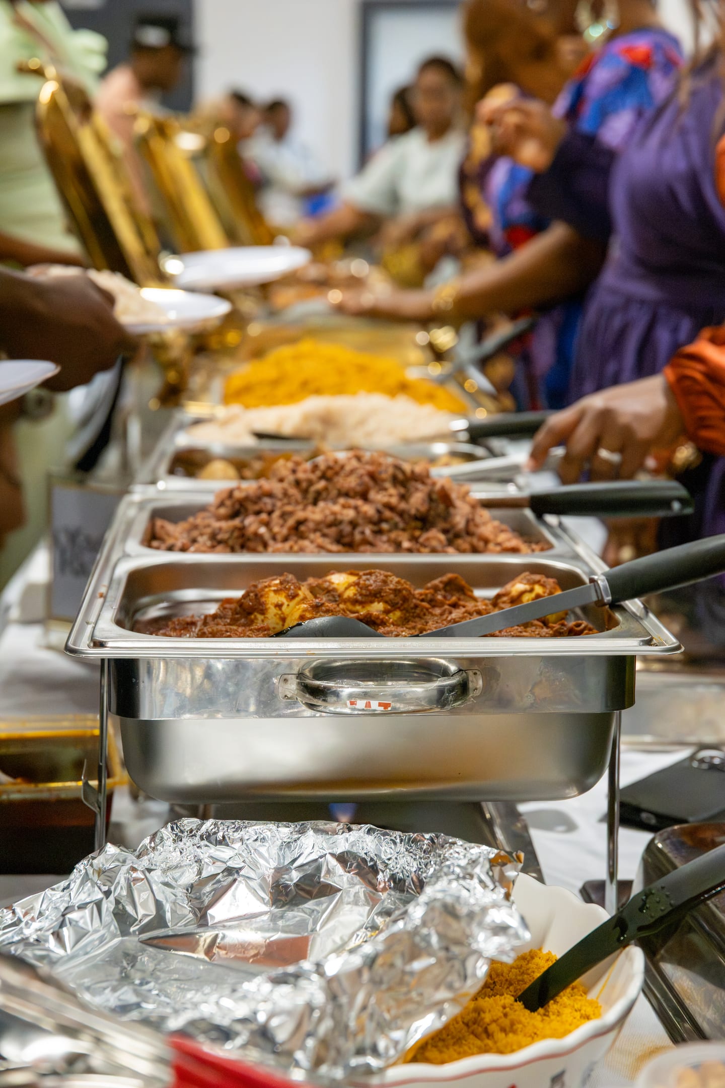 The buffet line in service, chafing dishes of jollof rice and stew being plated for a queue of guests